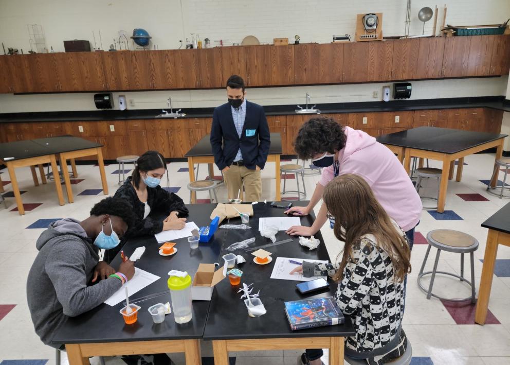Group of people with masks working at a table doing an experiment. 