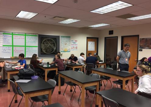 Dr. Kwon walking around a high school classroom with students at tables.
