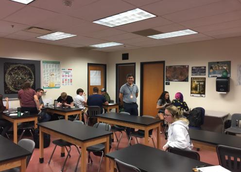Dr. Kwon smiling for a picture while he is standing in a high school classroom.