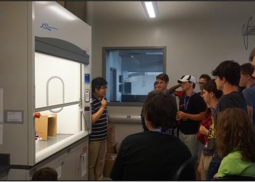 Students listening to a speaker who is showing them lab equipment.