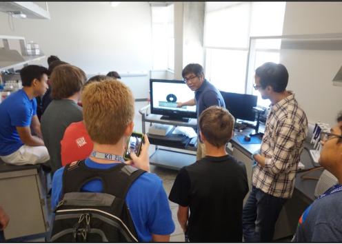 Group of high school students crowded around lab computer. 